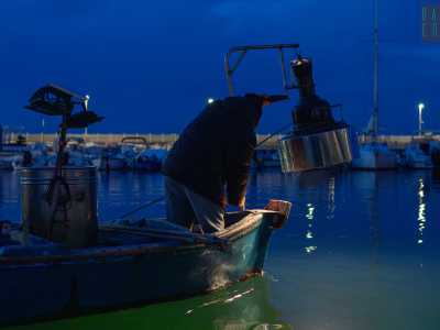 La pesca inizia quando non siamo ancora usciti dal porticciolo. Giuseppe a poppa si posiziona accanto alla lampara accesa...